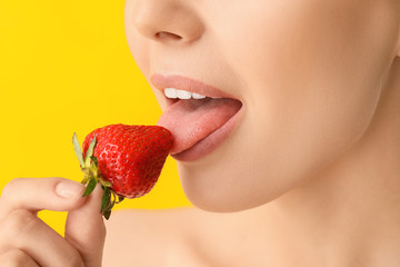 Sexy young woman with strawberry on color background, closeup