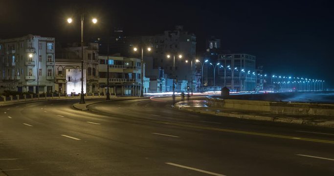 Night time-lapse of a road along the El Malecon waterfront in Havana Cuba, with old apartment buildings in the background.