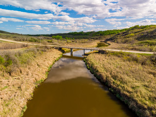 an aerial view of a rural bridge over a peaceful secluded stream hidden in the valleys of the Saskatchewan Prairies