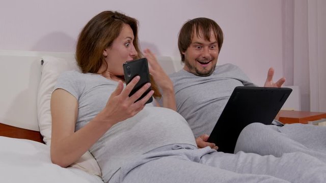 Happy couple holding smartphone looking at cellphone screen watching, be surprised on sofa, having fun enjoy read online news in smartphone at home.