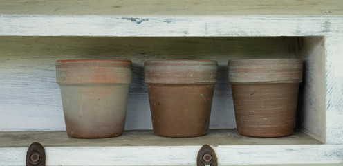 Close up of potting bench showing three small clay pots on a shelf. Stay at home gardening concept.