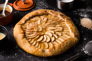 Pizza doce de creme com maça e cobertura de caramelo sobre a mesa de cor preta com acessórios - Borda açucarada, caçarola laranja com caramelo