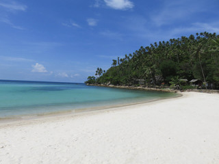 White sandy beach with Thailand with green palm trees and blue ocean in the background.