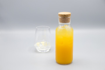 Glass bottle with cork of freshly made orange juice with ice and a cup near.