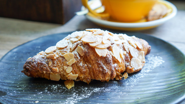Almond Croissant in black plate on a cafe table with blurred background of yellow coffee cup