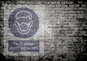 Grunge decayed faded brick wall background with face mask must be worn sign with copy space for own text  