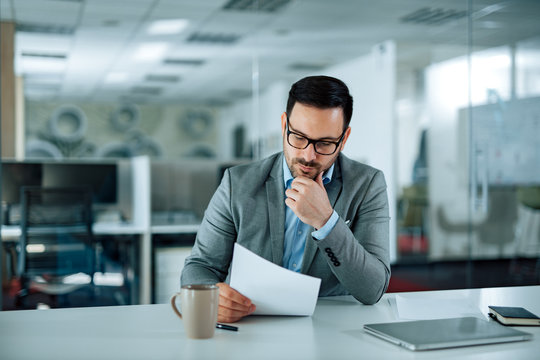 Pensive businessman at work. Handsome man in formal wear looking at document in the office.
