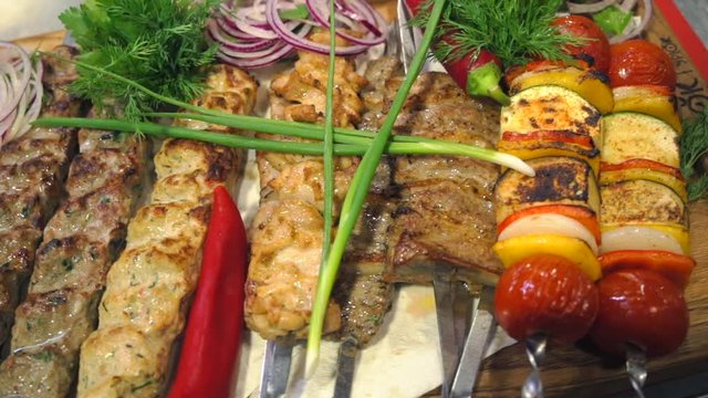 Serving kebabs in a meat restaurant. Shish kebab dish. Meat and vegetable kebabs on a wooden dish. Food video close up slow motion.