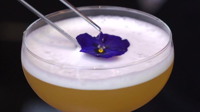 The process of making a cocktail. The barman's making a cocktail at the bar. The close-up of the cocktail preparation. An alcoholic cocktail is decorating with a flower.
