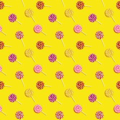 Seamless pattern with sweet round candy lollypops with stripes on stick on yellow paper background....