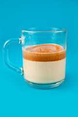 Glass cup of whipped dalgona coffee on a blue background.
