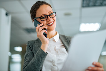 Close-up portrait of a smiling woman talking on smart phone and looking at document.