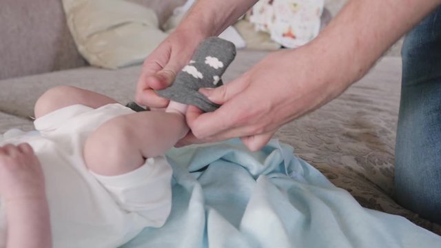 Dad puts a sock on the foot of a newborn. newborn baby lies on bed close up