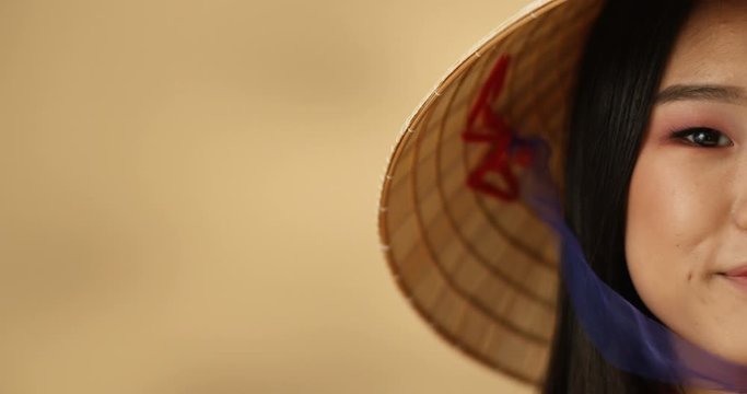 Close up of half face of young Asian beautiful woman smiling to camera joyfully. Happy pretty girl in Chinese conus hat with cheerful sincere smile.