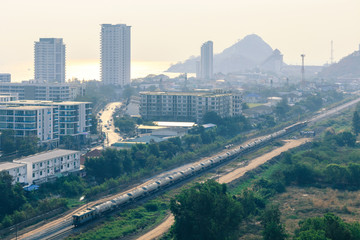 Naklejka premium aerial view of train running through small city by the sea in morning sunlight with reflection on water, city in poor weather morning, haze of pollution covering city