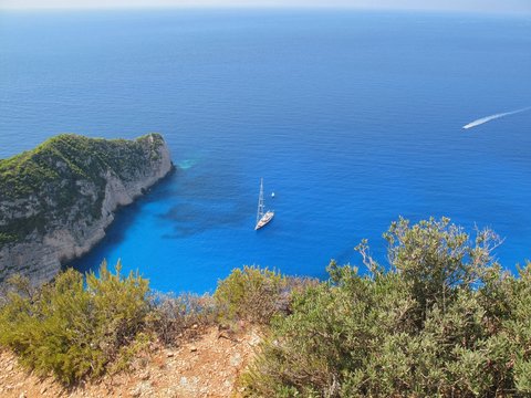 Beautiful panoramic view from the rock cliff to the amazing blue bay with sailboat, Zakyntos island, Greece.