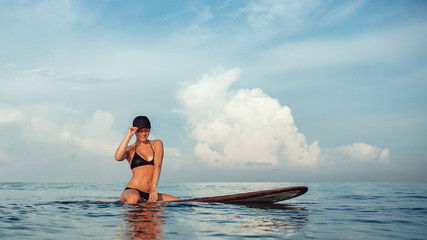Obraz premium Beautiful girl posing sitting on a surfboard in the ocean