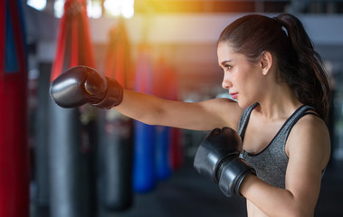Boxer woman during boxing exercise making direct hit with black gloves isolated on boxing gym background.