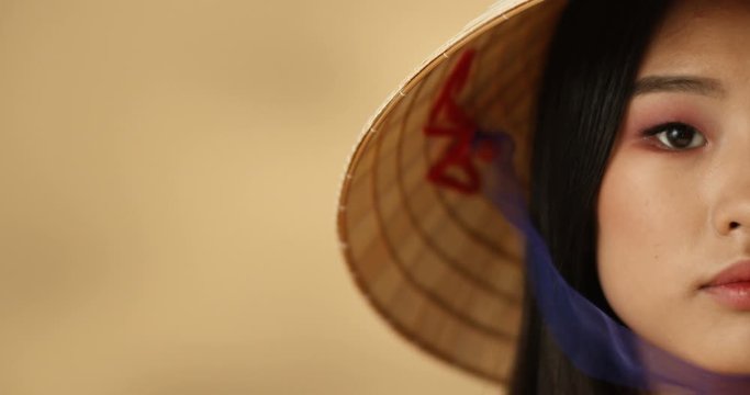 Close up of half face of young Asian beautiful woman looking seriously to camera. Portrait of serious pretty girl in Chinese conus hat with look straight and strict.
