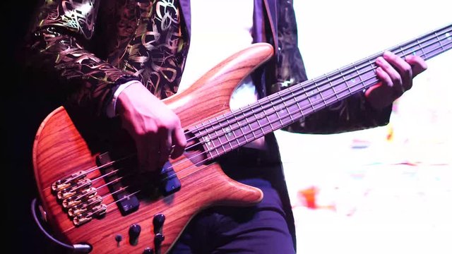 A bass guitarist playing electric bass guitar in the concert band entertaining audiences