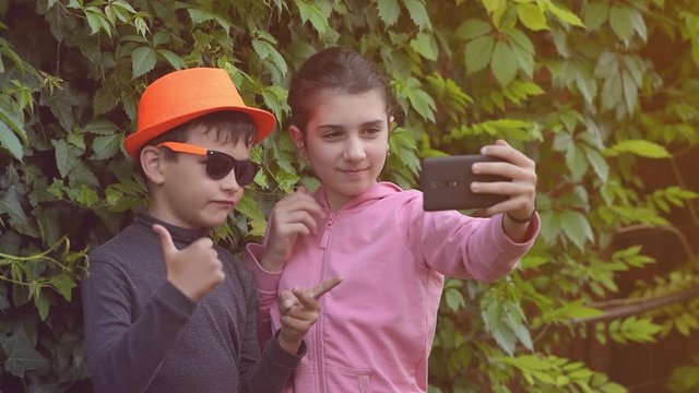 a boy and a girl take funny, emotional selfies on a smartphone, a brother and sister dance and make faces while taking pictures of themselves on a phone camera