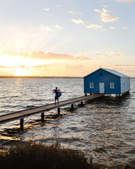 Man standing at the blue boat house with an australian flag on his back. 