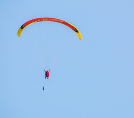 Orange and yellow paraglider on clear blue sky