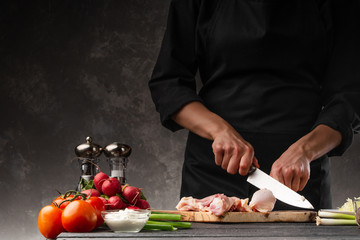 A chef cuts a chicken leg for cooking meat dishes. Cooking and cooking. Culinary blog or cooking show.