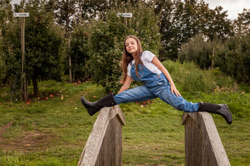 portrait of a young beautiful girl posing on the old wood bridge in green autumn farm.