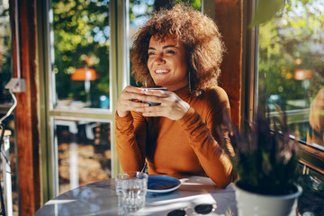 Young attractive mixed race woman sitting in cafe and enjoying coffee.