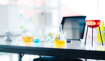 Modern science research lab with beaker glass and colorful sample liquid on table in white blur background, Experimental human vaccine for clue coronavirus or covid 19