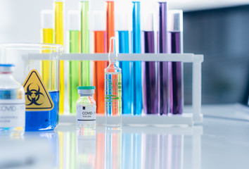 Modern science research lab with beaker glass and colorful sample liquid on table in white blur background, Experimental human vaccine for clue coronavirus or covid 19