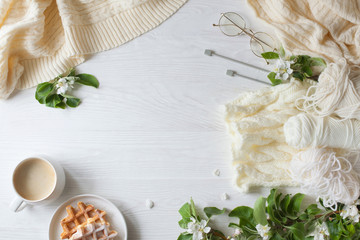 Knitting, knitting needles, yarn, coffee and waffles stand on a white wooden background. Surrounded...