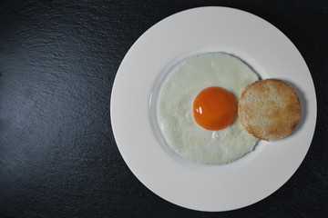 Breakfast of eggs on a white plate and black stone. Top view with copy space. Healthy eating