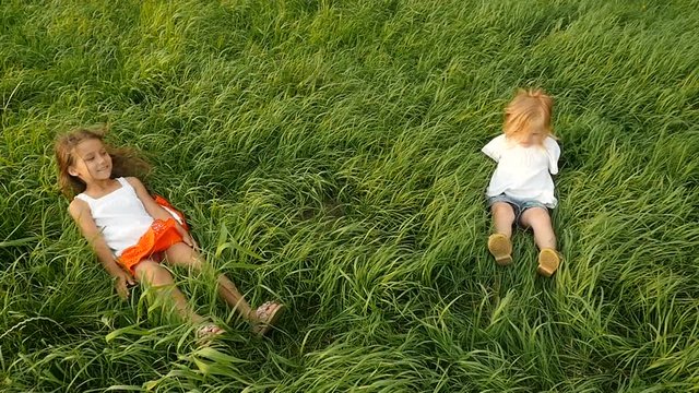 Cute little girls falling on green grass and lying