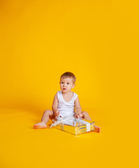 a little boy sits in a T-shirt and underpants next to a big gift box.