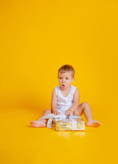 a little boy sits in a T-shirt and underpants next to a big gift box.