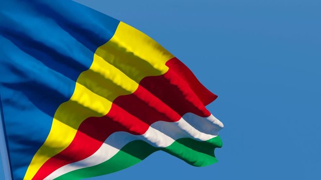 The national flag of Seychelles flutters in the wind against a blue sky