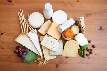 High protein foods. Assorted sliced and whole cheeses, bottle of milk, nuts and grape bunch on wooden table. Delicatessen and healthy eating concept
