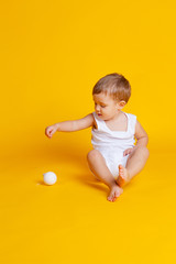 little boy in a t-shirt and underpants on an orange-yellow background with a white Christmas ball in his hand