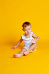 little boy in a t-shirt and underpants on an orange-yellow background with a white Christmas ball in his hand
