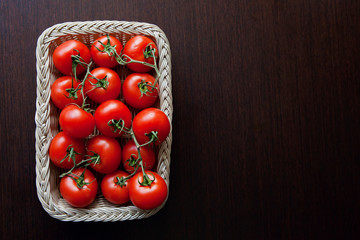 Tomatos in wicker tray on dark wooden background. Healthy food. Dietetic foods. Copy space