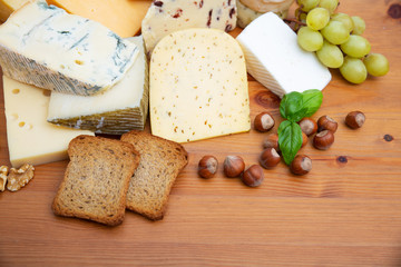 Blue and spicy different cheeses and snacks set. Slices of bread, grapes and nuts on brown wooden table. Top view, copy space. Cheese dairy concept