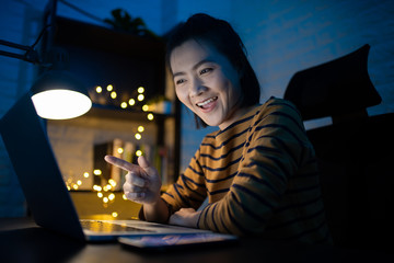 Asian woman happy smiling working on a laptop at the night at home. WFH. Work from home avoid COVID 19 concept.