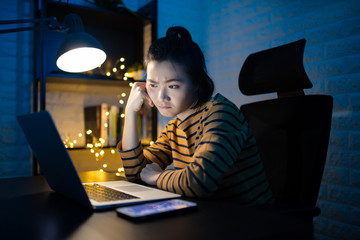 Asian woman bored working on a laptop overtime at home. WFH. Work from home for avoid the...