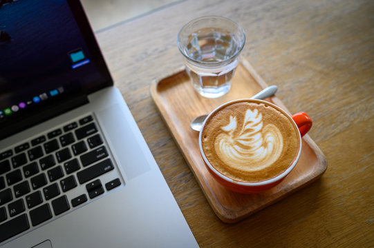 Latte art coffee cup on wooden table with lapop computer