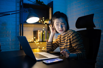 Asian woman feel confused scratching her head and working on a laptop overtime at home. WFH. Work...