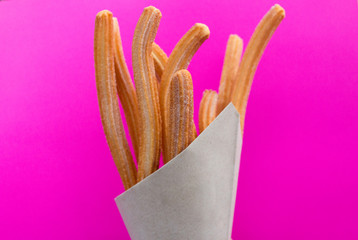 Churros with sugar in paper bag on pink background