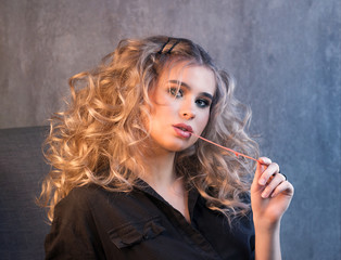 Obraz premium Portrait of a blonde girl with long and volume shiny wavy hair with chewing gum in her mouth. A woman is chewing gum. Stretching bubble gum.