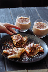 Woman's hand decorates pancakes with a fruits kiwi and banana, chocolate. Black plate, black table. Selective focus